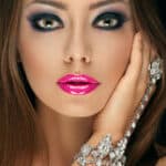 Primo piano di una ragazza con i capelli sciolti e una mano con gioielli sul lato del viso, con un trucco smokey eyes sul blu molto scuro e le labbra con il rossetto di un fucsia brillante
