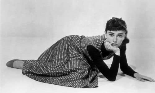 Foto di Audrey Hepburn sdraiata a terra con una mano sotto il mento e il volto imbronciato