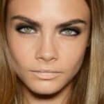 Foto in Primo piano della modella Cara Delevingne con un rossetto color carne lucido che uniforma le labbra con il colore della pelle.