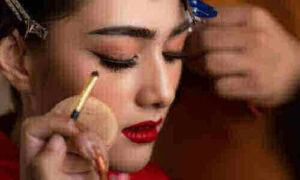 Donna viene truccata da un make up artist con un ombretto rosso