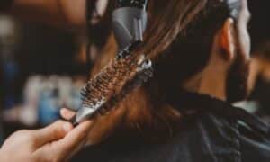 foto in primo piano di un parrucchiere che passo il phon sui capelli lunghi di un ragazzo, aiutandosi con una spazzola