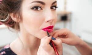 Make up artist applica un rossetto di un colore molto acceso per illuminare il volto della modella, con già un eyeliner nero che le ingrandisce l'occhio