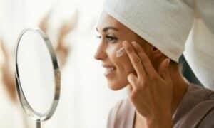 Donna si spalma la crema idratante sul viso davanti allo specchio