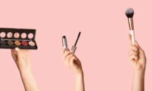 raffigurazione di tre mani che tengono in mano vari cosmetici su uno sfondo rosaato