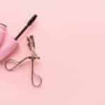 Sfondo rosa con piegaciglia dorato e mascara dalla confezione rosa confetto
