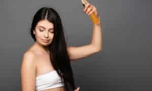 Foto di una ragazza con lunghi capelli neri che si applica sui capelli un prodotto per la protezione dal calore