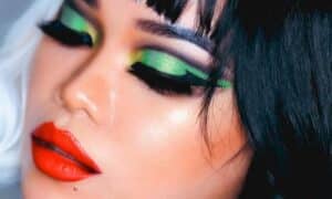 Foto in primo piano del volto di una modella truccata con un makeup punk neon, con colori forti come lime, giallo e una riga molto spesso di eyeliner nero, con labbra rosso acceso