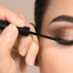 Foto in primo piano di un occhio truccato in cui viene applicata una linea finissima di eyeliner nero