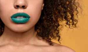 primo piano delle labbra di una modella dal colore della pelle più bronzeo che ci dimostra come potersi permettere un rossetto di un colore acceso come il verde acqua