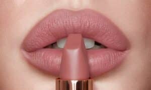 Foto in primo piano di un rossetto mat nude poggiato su labbra semiaperte truccate dello stesso colore