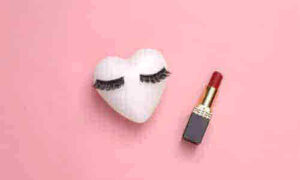 sfondo rosa con un cuore bianco con sopra le ciglie finte, tipiche del trucco anni venti e il rossetto rosso