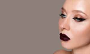 primo piano di una donna con le labbra dal rossetto bordeaux e una sfumatura di ombretto rosso aranciaco con eyeliner