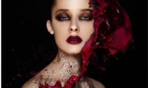 modella con glitter neri e rossi sul collo e un grande fiore rosso al lato del viso, sfoggia un trucco molto drammatico rosso e nero
