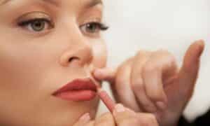 Make-up artist trucca con una matita rosa pesca le labbra di una donna con un trucco shimmer con toni oro e marroni per evidenziare gli occhi verdi 